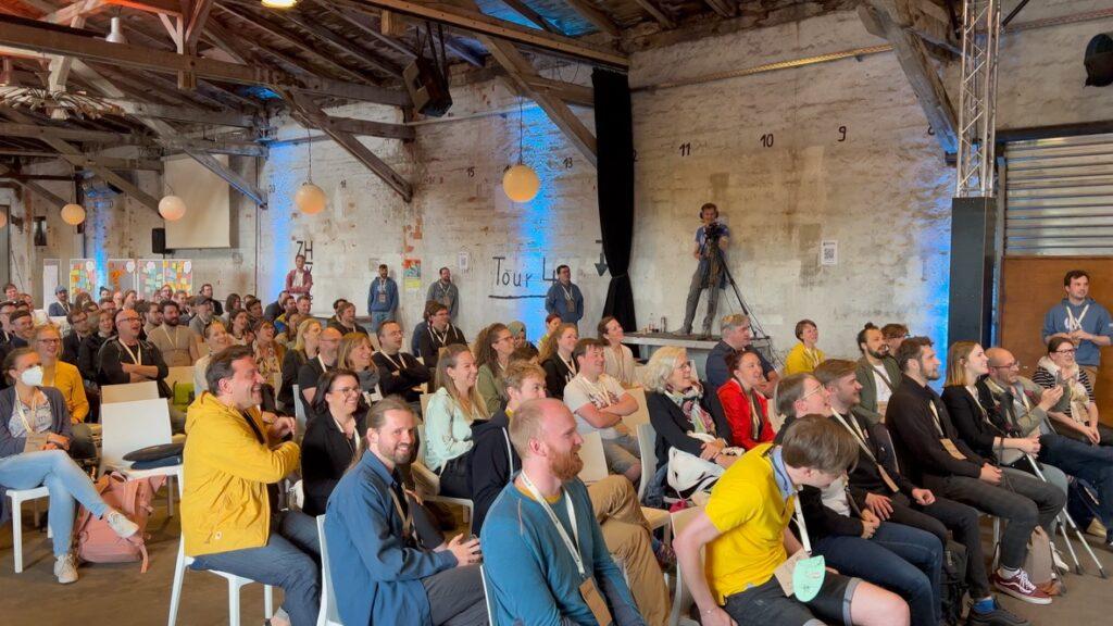 Viele Menschen sitzen auf Stühlen vor einer Bühne